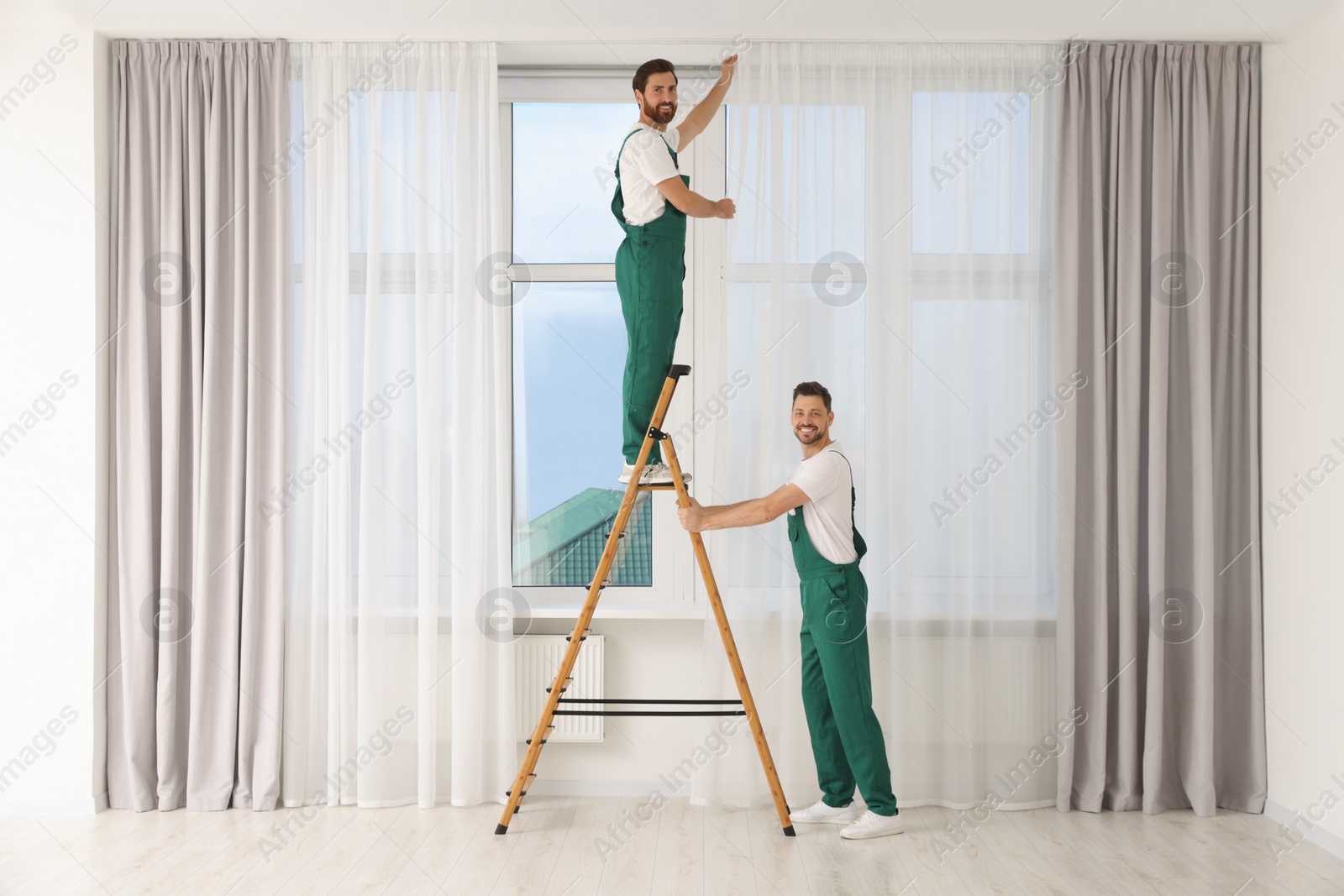 Photo of Workers in uniform hanging window curtain indoors