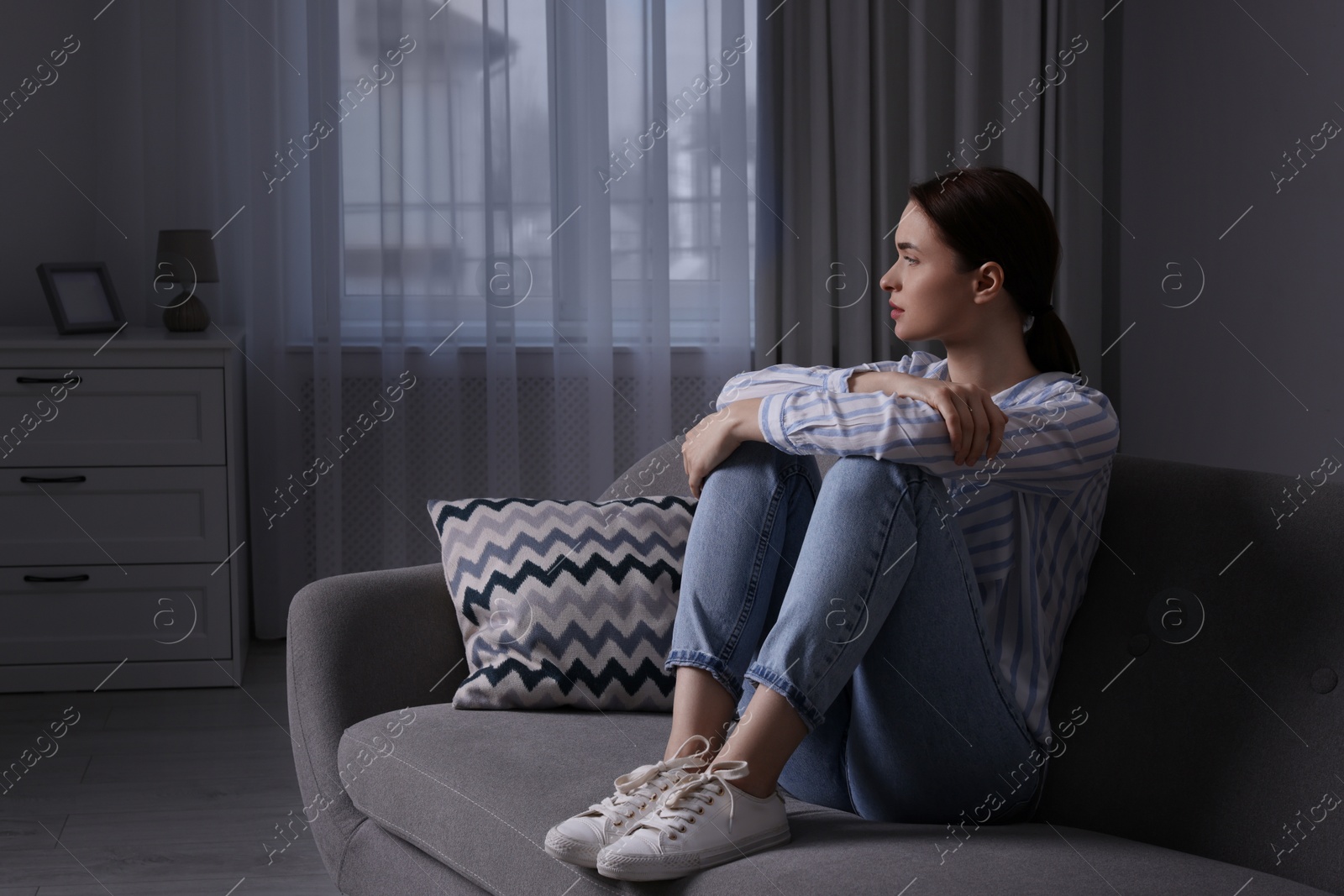 Photo of Unhappy young woman on sofa at home, space for text. Loneliness concept