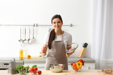 Young woman cooking tasty soup in kitchen