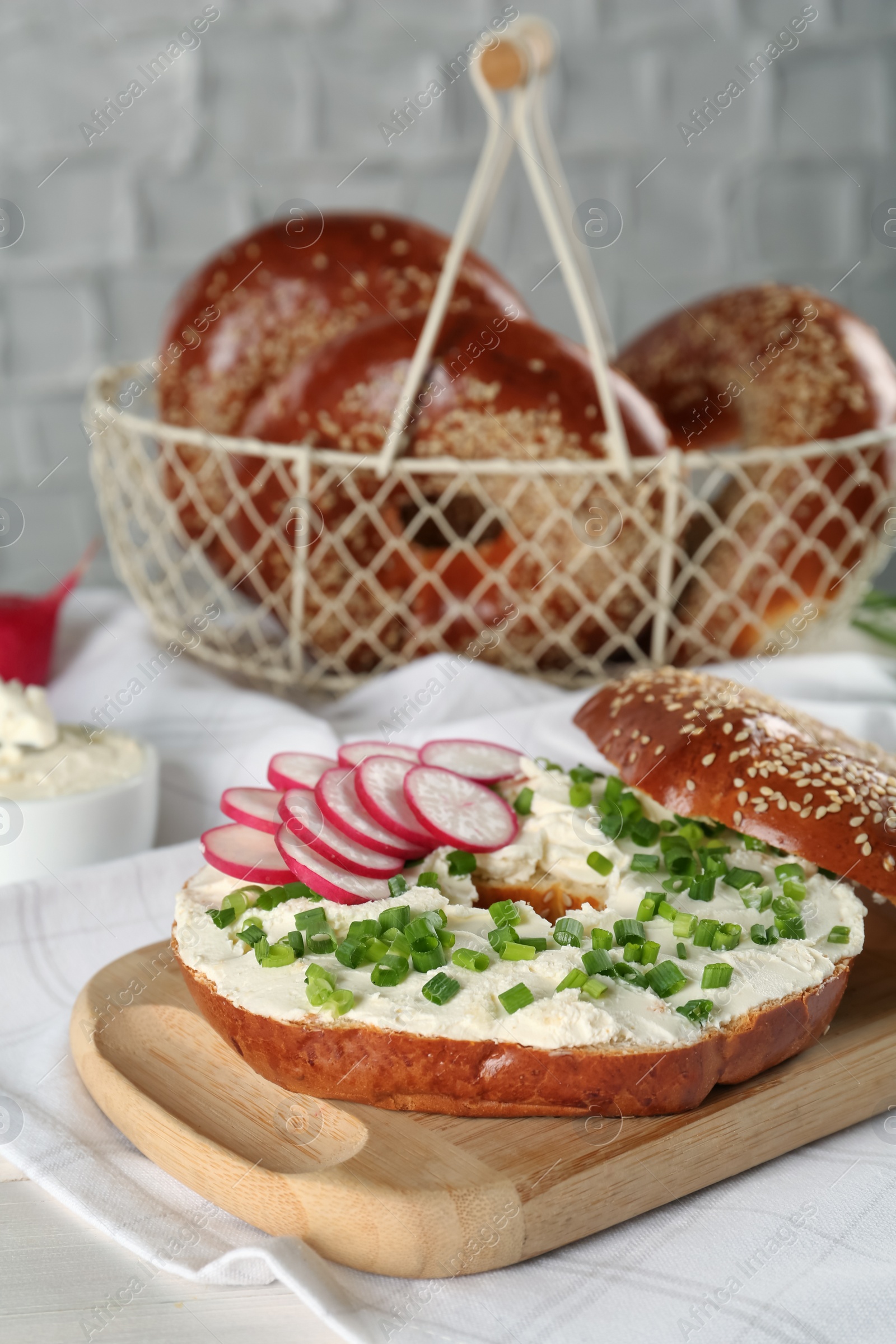 Photo of Delicious bagel with cream cheese, radish and green onion on white wooden table