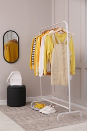 Rack with stylish women's clothes, backpack and shoes near light wall in dressing room