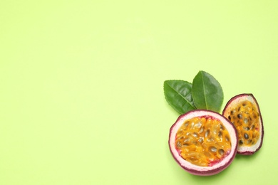 Slices of fresh ripe passion fruit (maracuya) with leaves on light green background, flat lay. Space for text