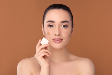 Photo of Woman applying foundation on face with makeup sponge against brown background