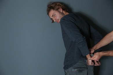 Photo of Man putting handcuffs on drug dealer against grey background. Space for text