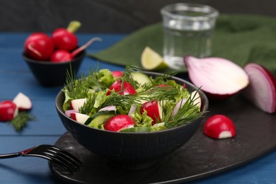 Tasty salad with radish in bowl on blue wooden table