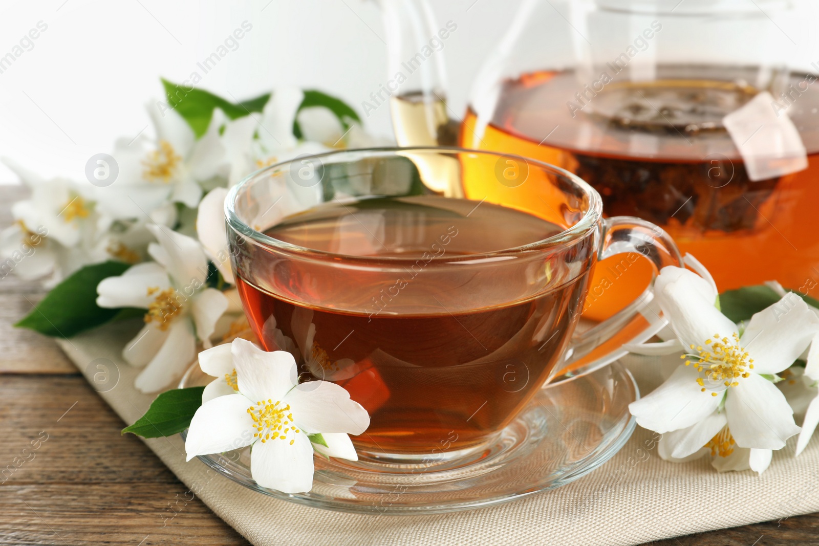 Photo of Aromatic jasmine tea and fresh flowers on wooden table, closeup