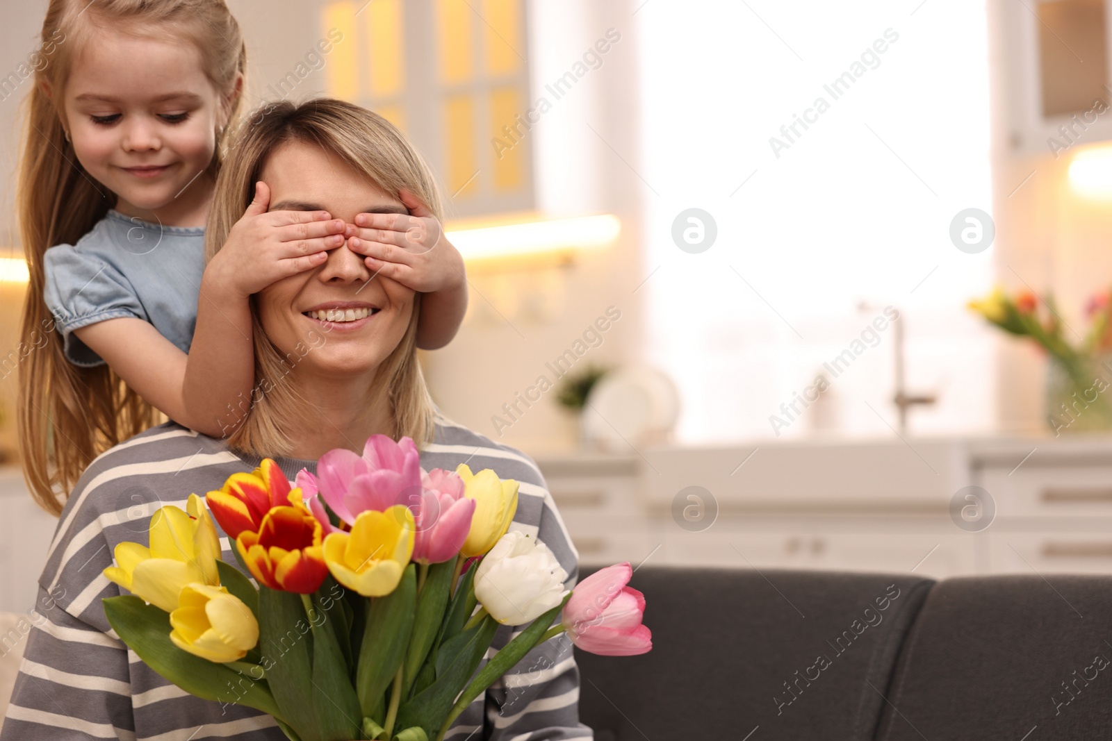 Photo of Little girl surprising her mom with bouquet of tulips at home, space for text. Happy Mother`s Day