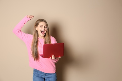 Photo of Emotional young woman with laptop celebrating victory on color background. Space for text