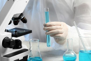 Photo of Scientist with test tube of light blue liquid near microscope in laboratory, closeup