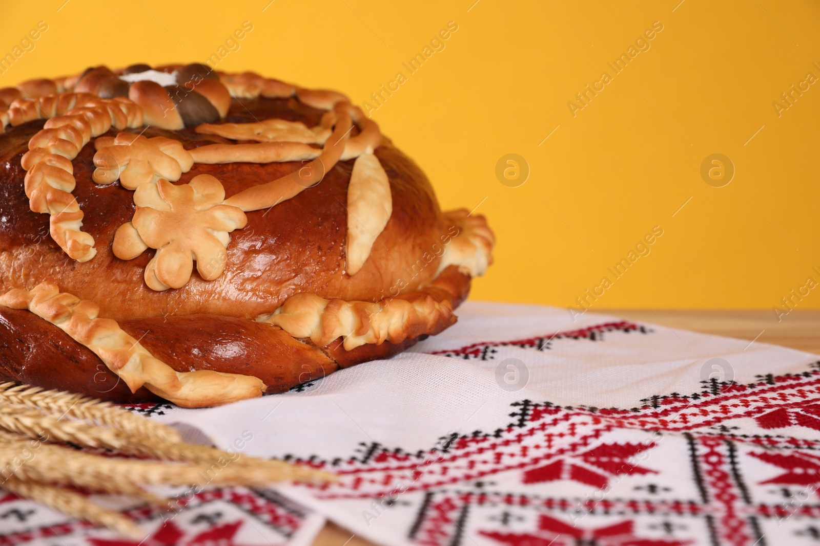 Photo of Rushnyk with korovai, wheat spikes on yellow background, closeup. Ukrainian bread and salt welcoming tradition