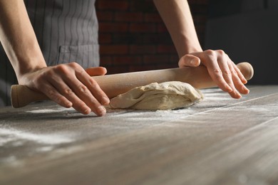 Photo of Making bread. Woman rolling dough at wooden table indoors, closeup