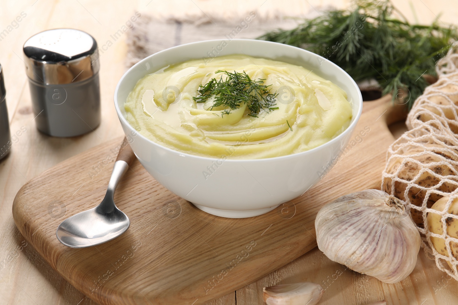 Photo of Bowl of tasty cream soup with dill, spoon and garlic on wooden table