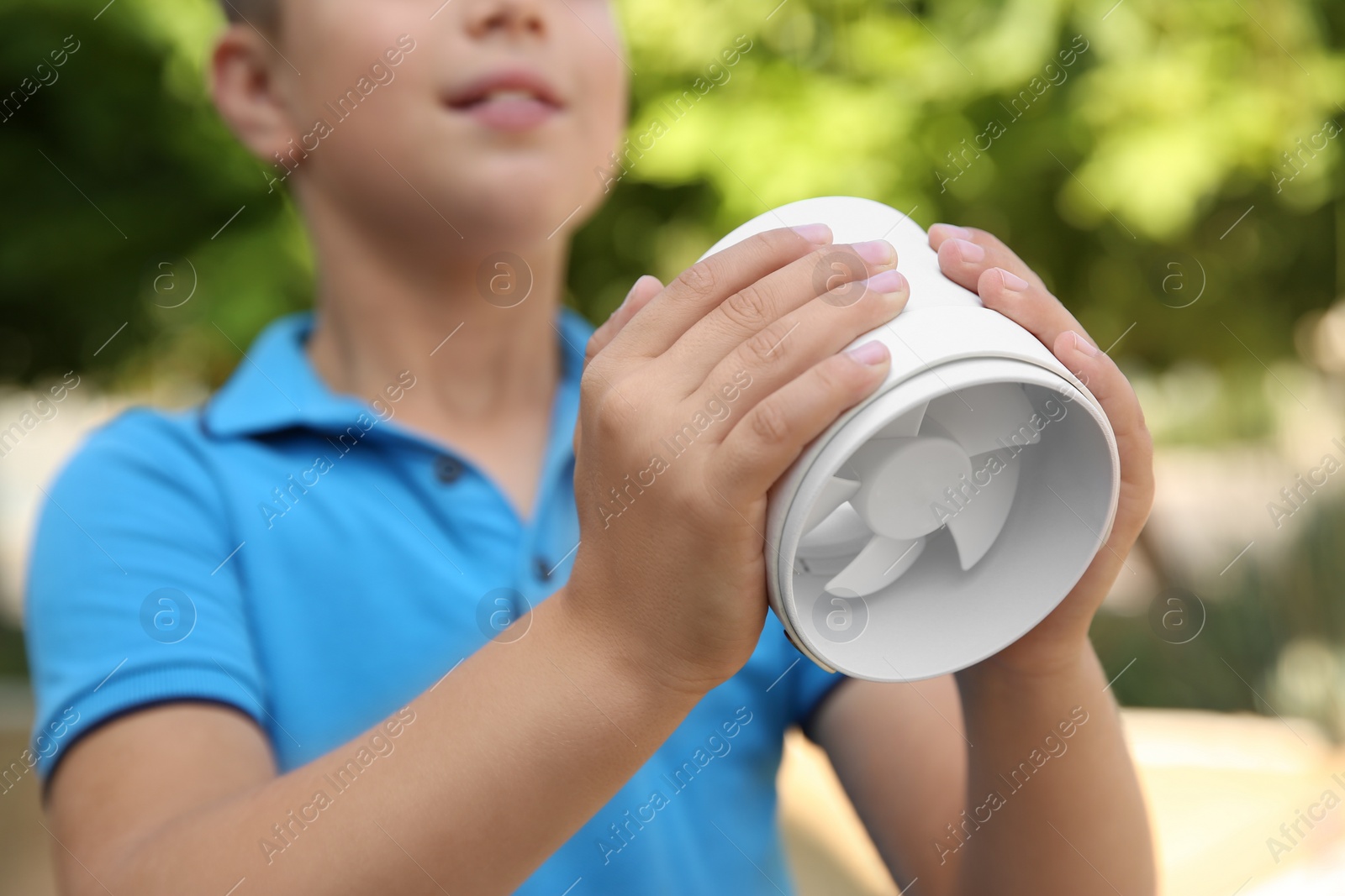 Photo of Little boy with portable fan outdoors, closeup. Summer heat