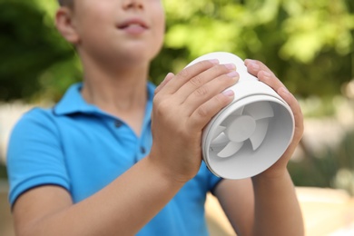 Little boy with portable fan outdoors, closeup. Summer heat