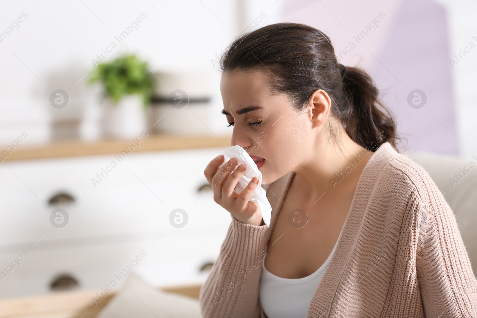 Photo of Young woman suffering from runny nose in living room