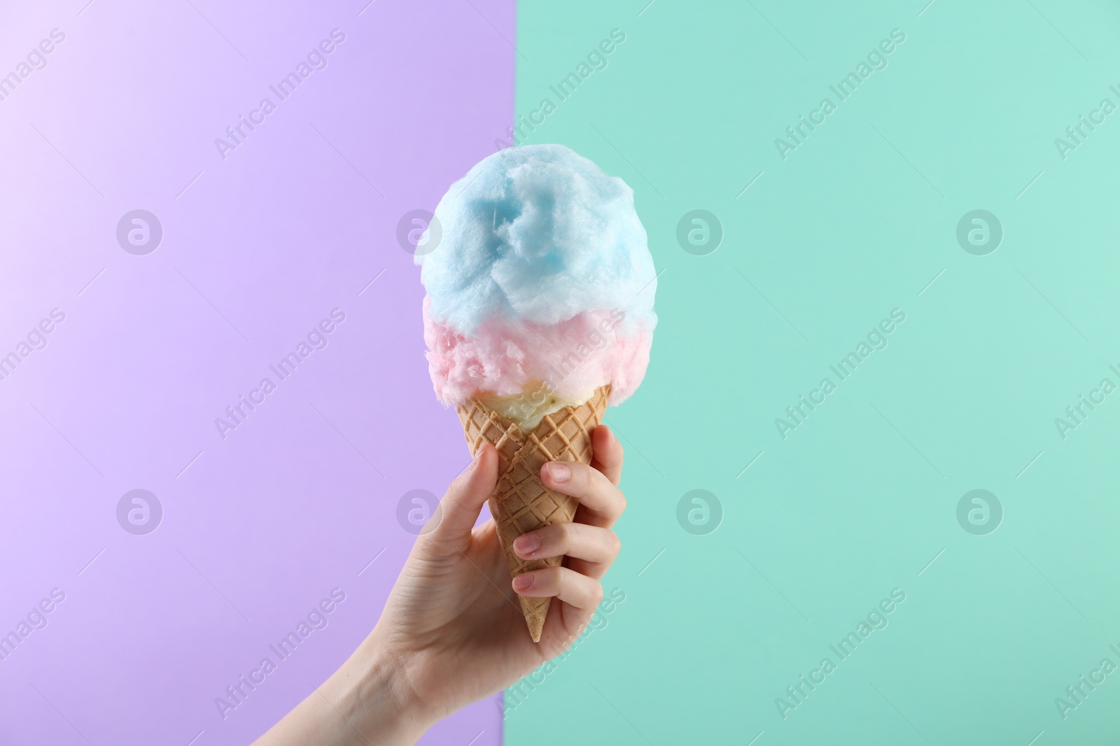 Photo of Woman holding waffle cone with cotton candy on color background, closeup