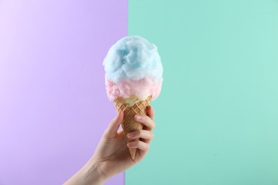 Photo of Woman holding waffle cone with cotton candy on color background, closeup