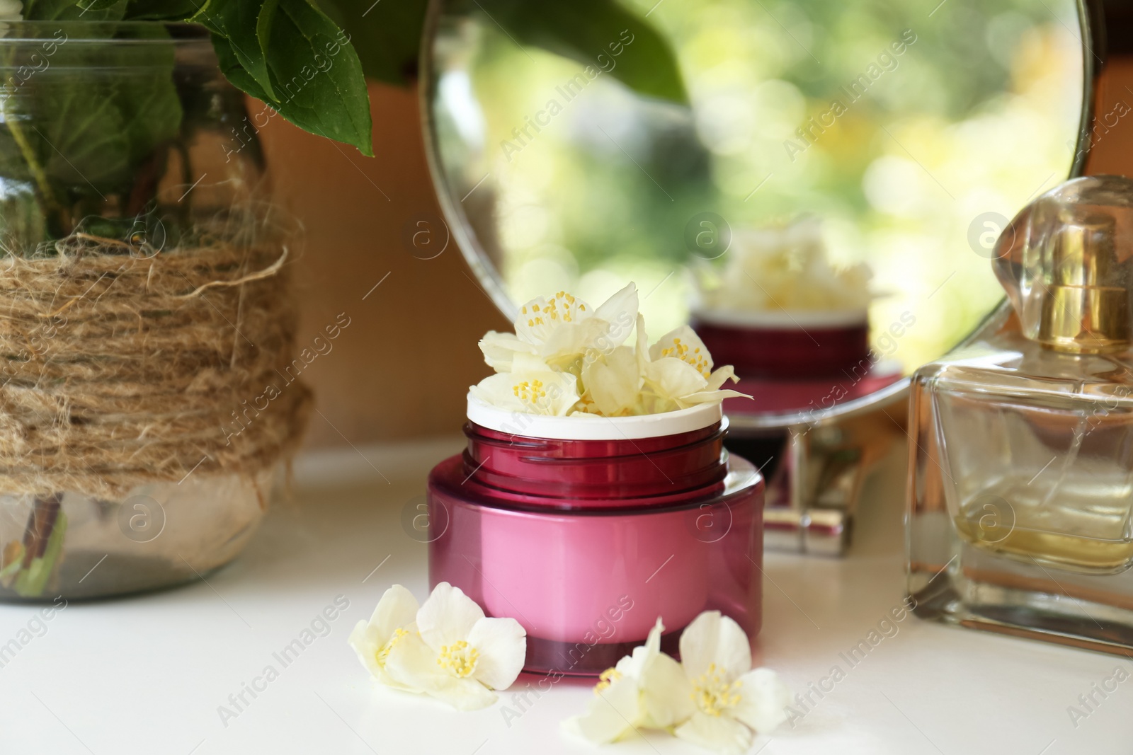 Photo of Jar of cream with beautiful jasmine flowers, perfume and mirror on white table