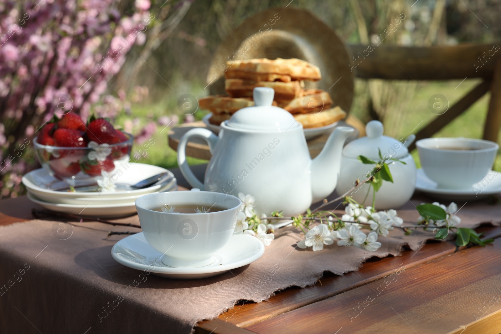 Photo of Beautiful spring flowers, freshly baked waffles and ripe strawberries on table served for tea drinking in garden