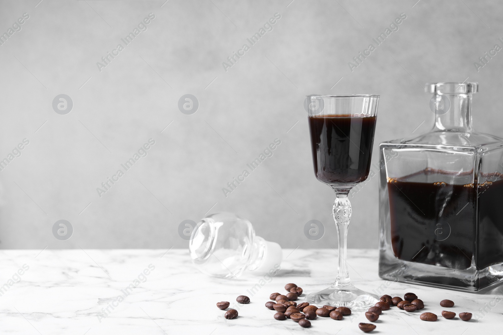 Photo of Coffee liqueur and beans on white marble table. Space for text