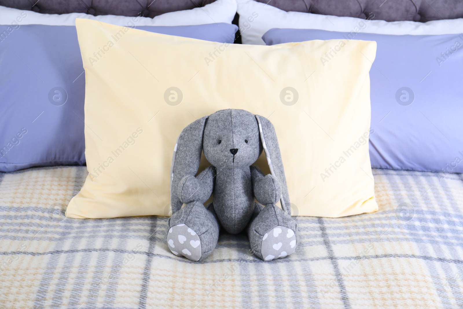 Photo of Cute toy rabbit sitting on bed indoors