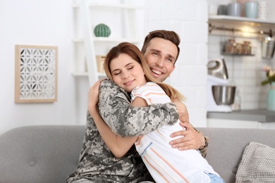 Photo of Young man in military uniform with his wife on sofa at home