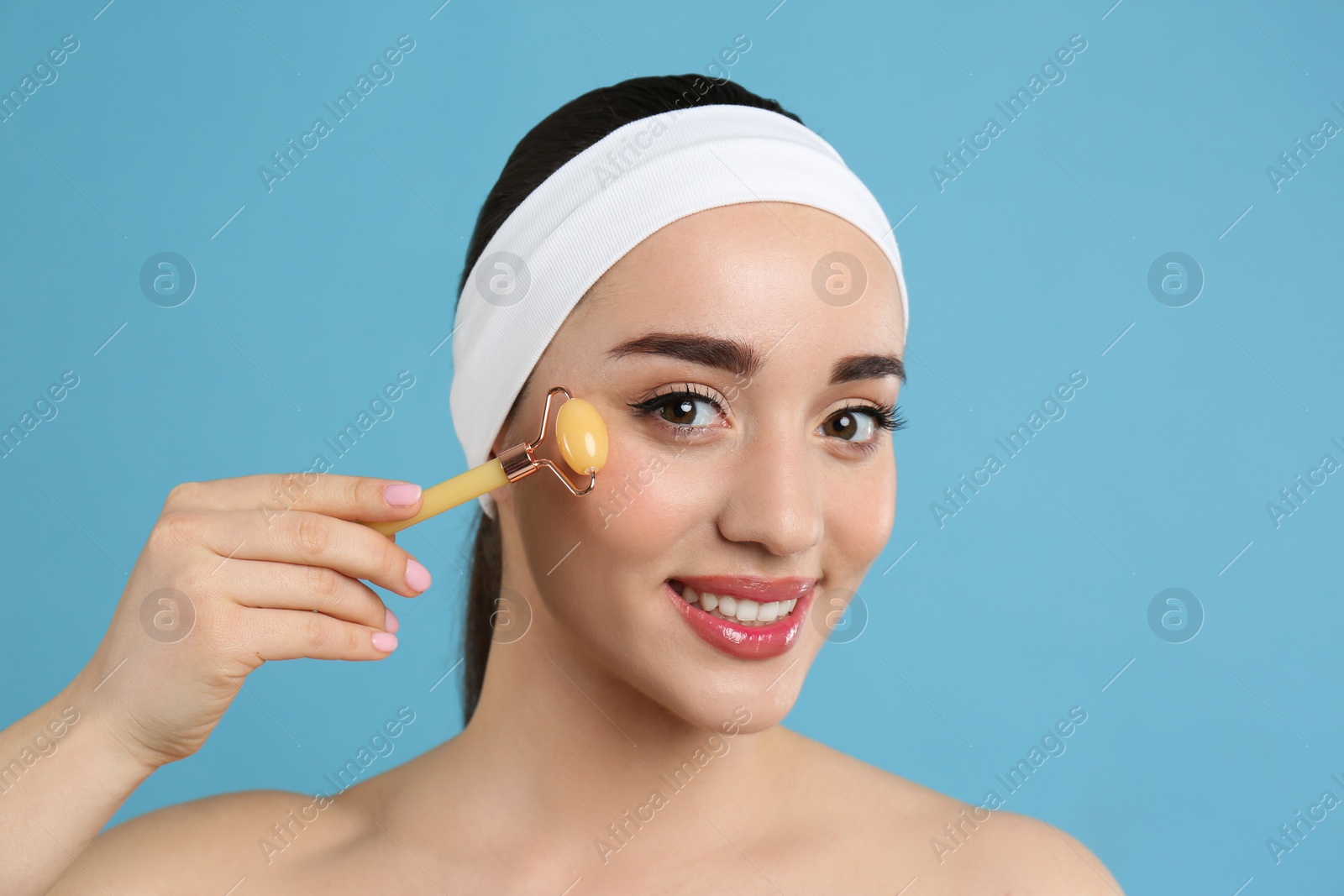 Photo of Woman using natural face roller on light blue background