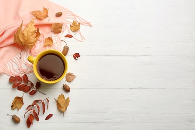 Photo of Flat lay composition with cup of hot drink and autumn leaves on white wooden table, space for text. Cozy atmosphere