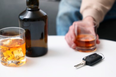 Man holding glass of alcoholic drink at table with car keys, closeup. Don't drink and drive concept