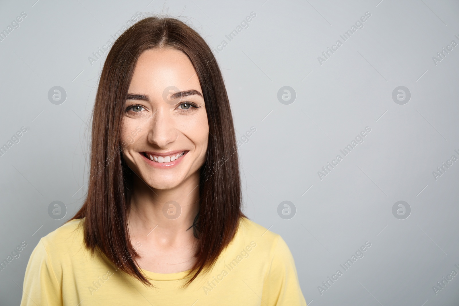 Photo of Portrait of pretty young woman with gorgeous chestnut hair and charming smile on light grey background, space for text