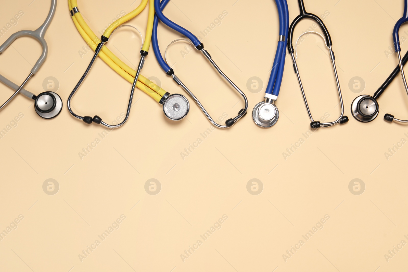 Photo of Stethoscopes on beige background, flat lay. Space for text