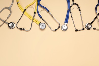 Photo of Stethoscopes on beige background, flat lay. Space for text