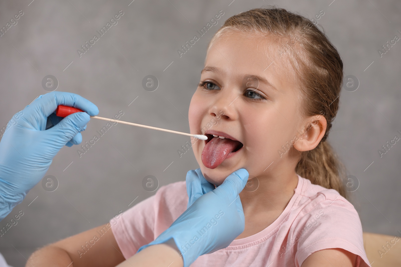 Photo of Doctor taking throat swab sample from girl`s oral cavity on grey background, closeup