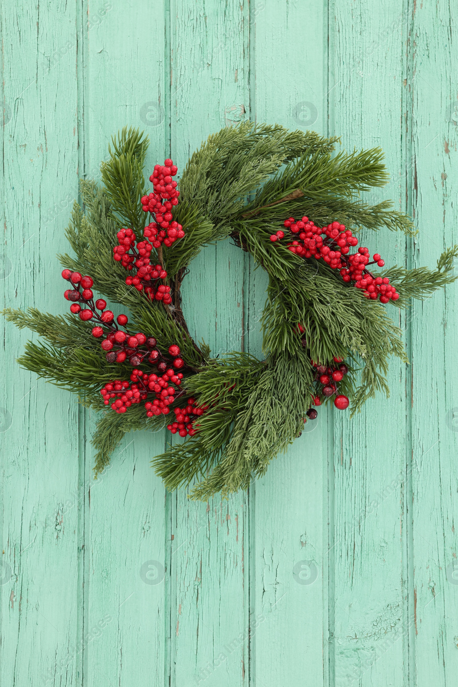 Photo of Beautiful Christmas wreath with red berries hanging on turquoise wooden wall