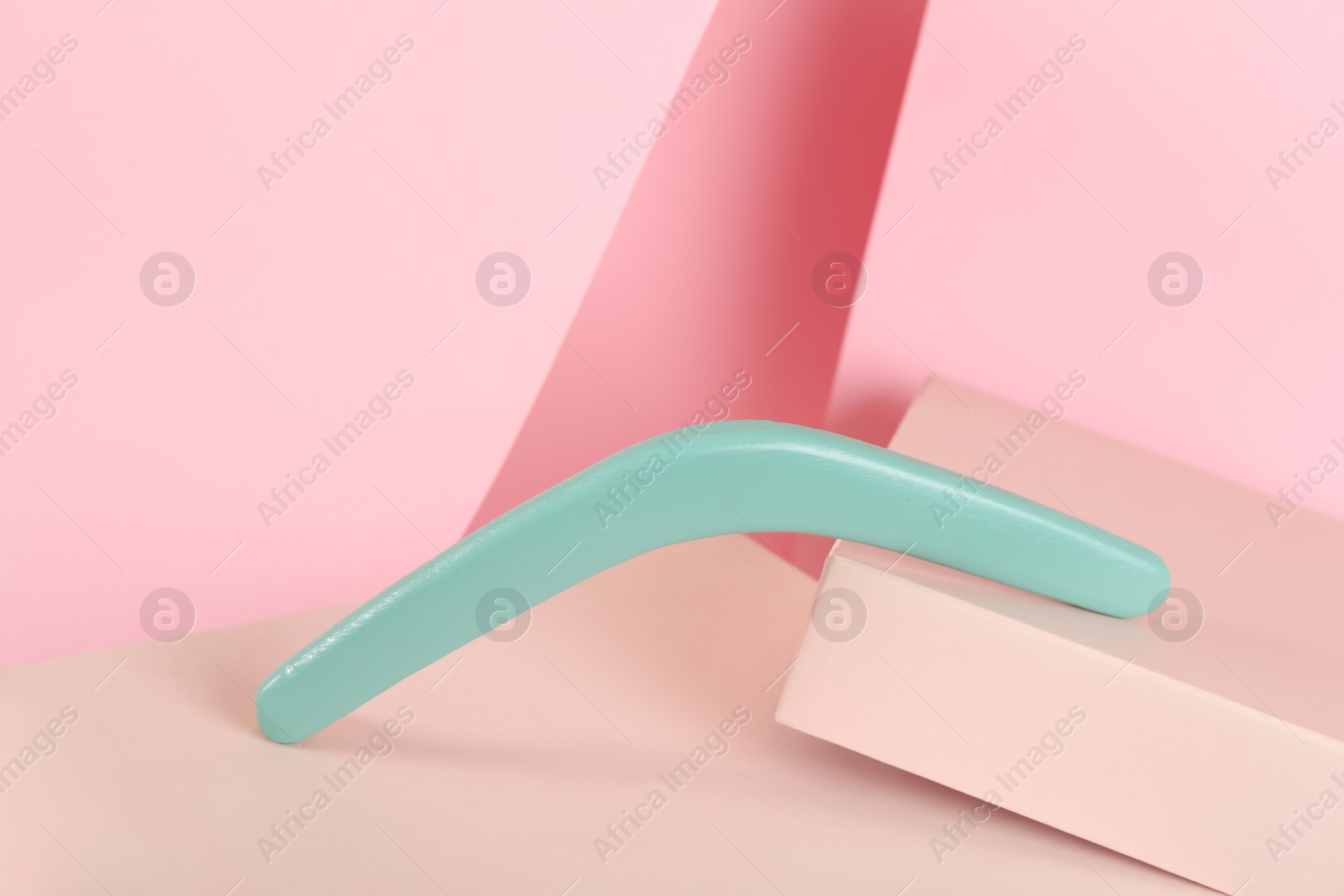Photo of Creative composition with turquoise wooden boomerang on pink background