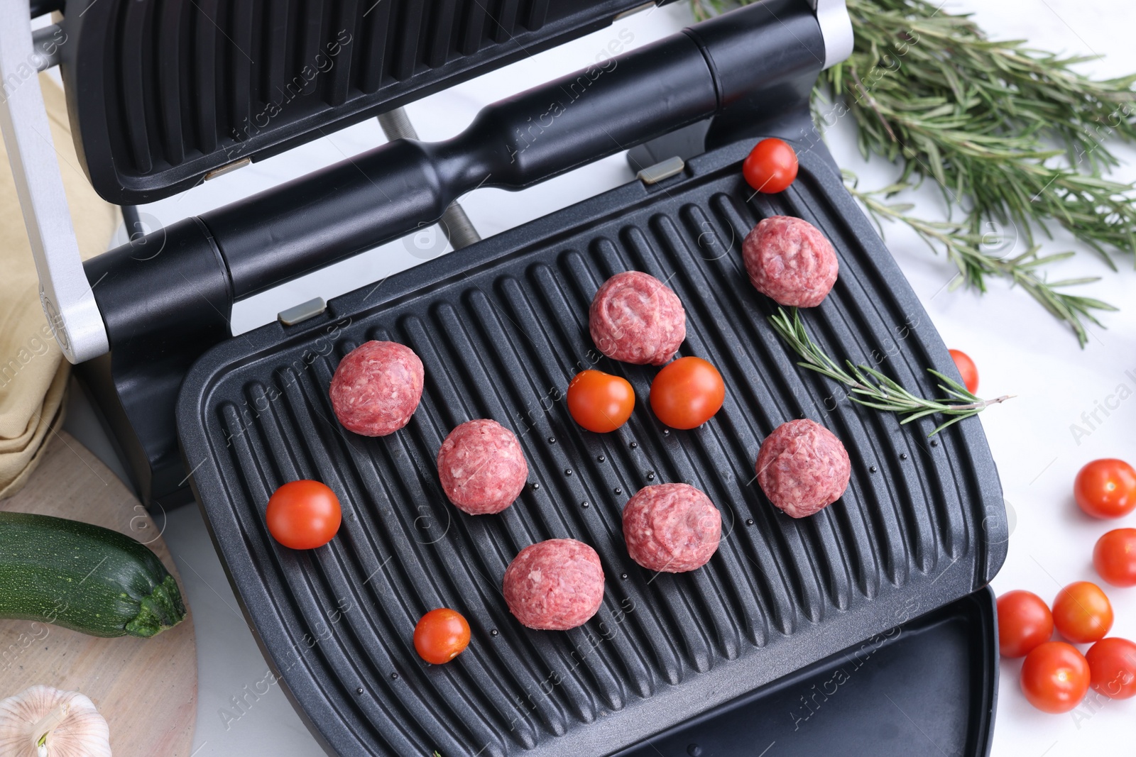 Photo of Electric grill with meatballs, tomatoes and rosemary on white table, above view