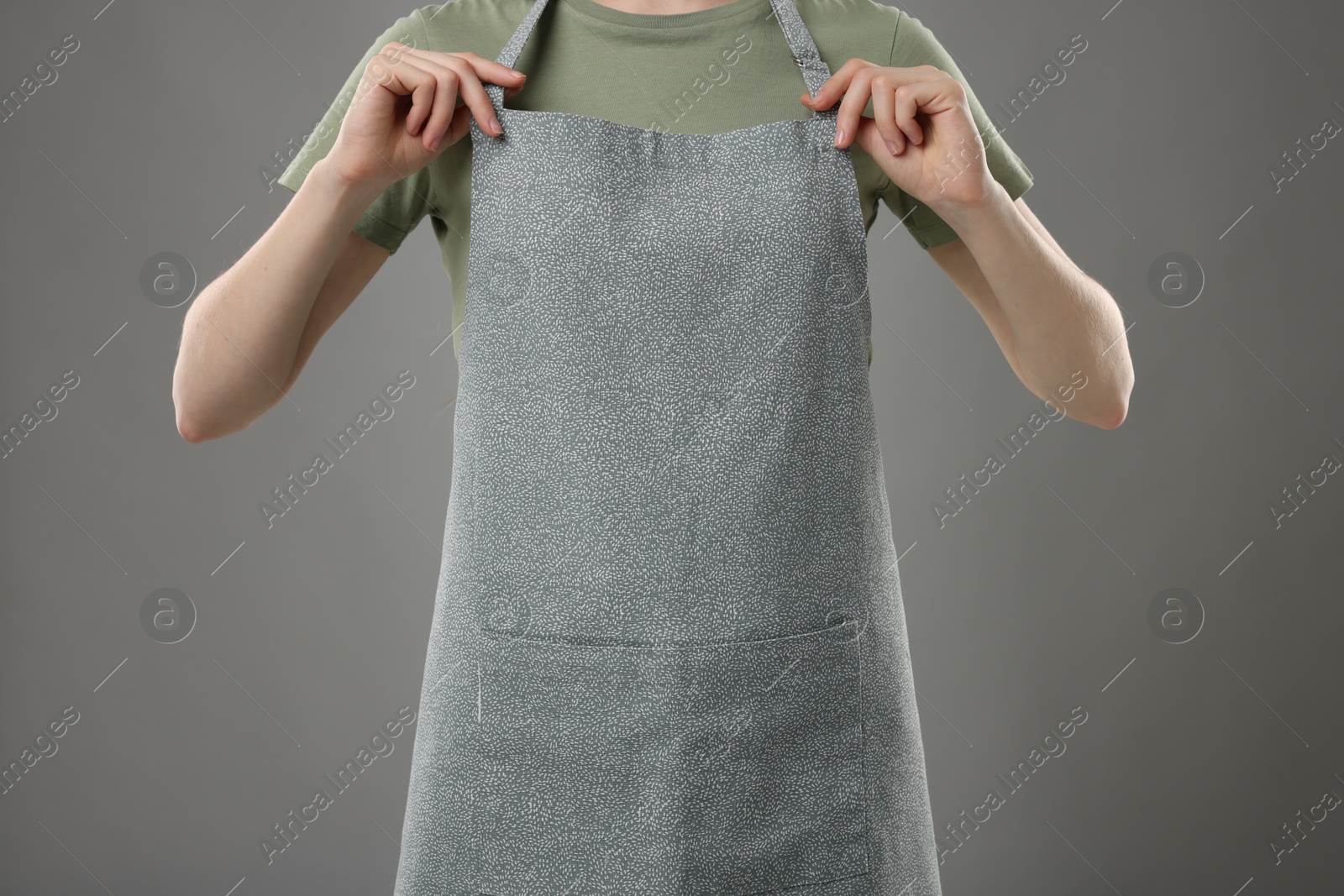 Photo of Woman wearing kitchen apron on grey background, closeup. Mockup for design