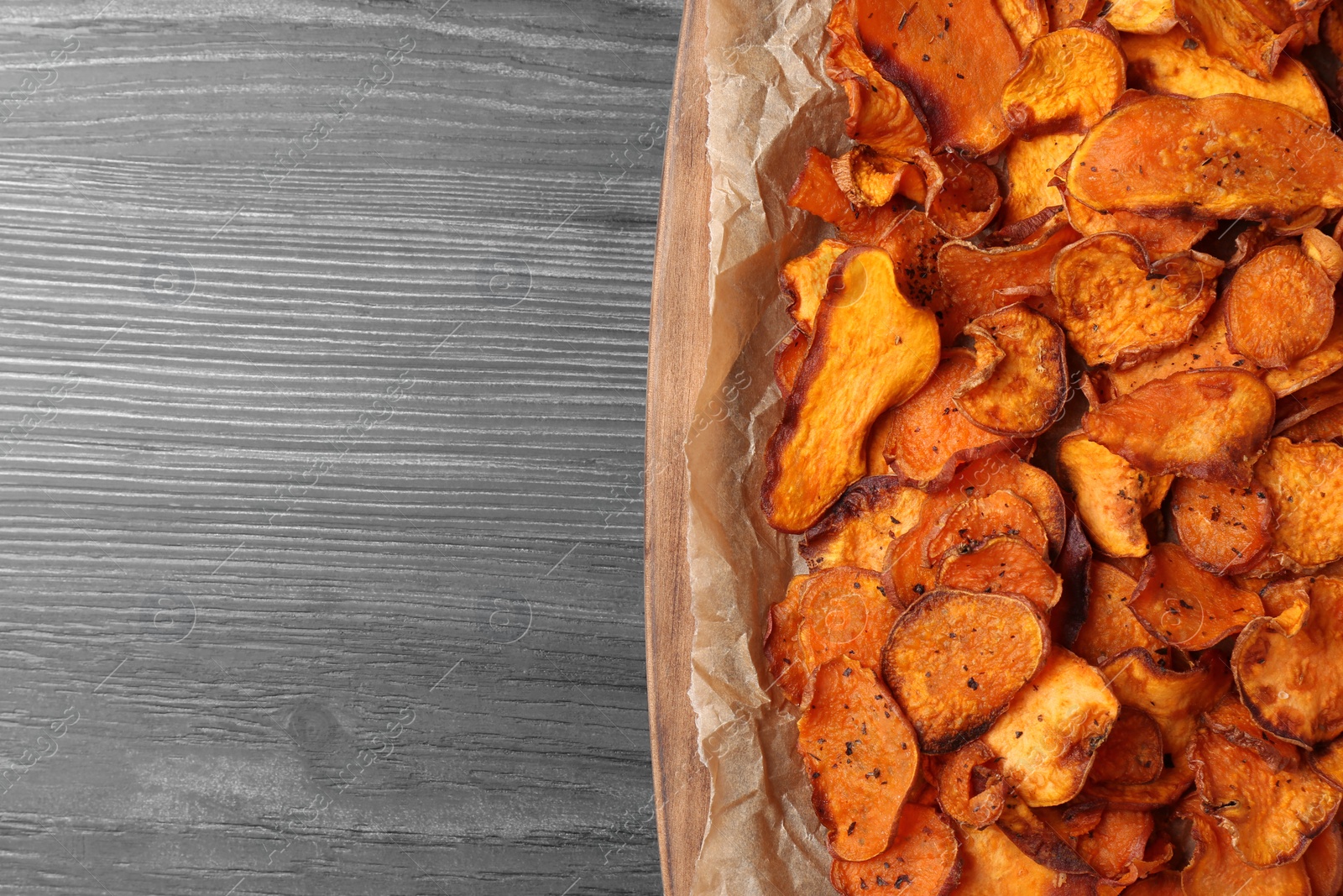 Photo of Tray with sweet potato chips on wooden table, top view. Space for text