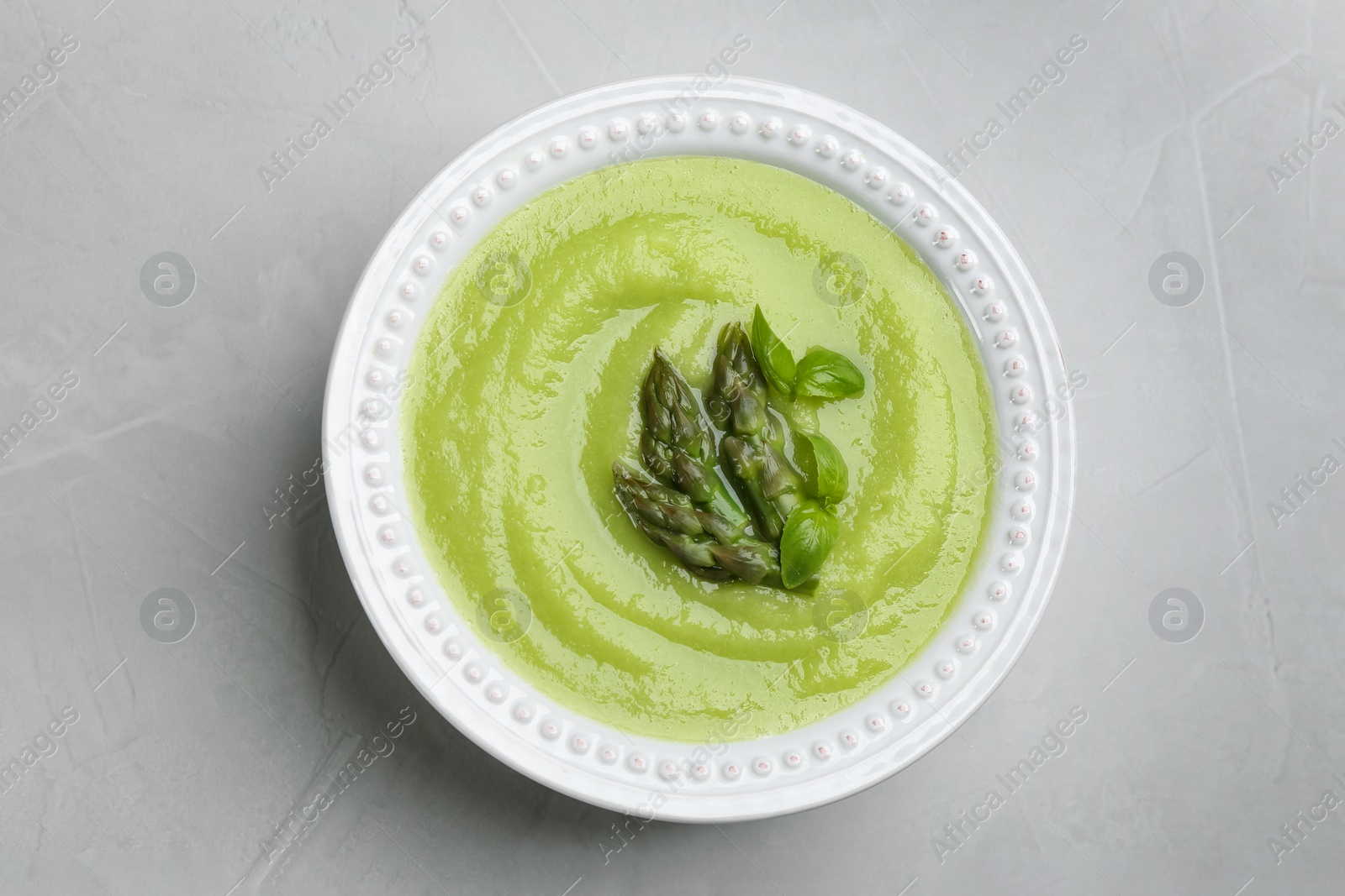 Photo of Delicious asparagus soup on grey table, top view