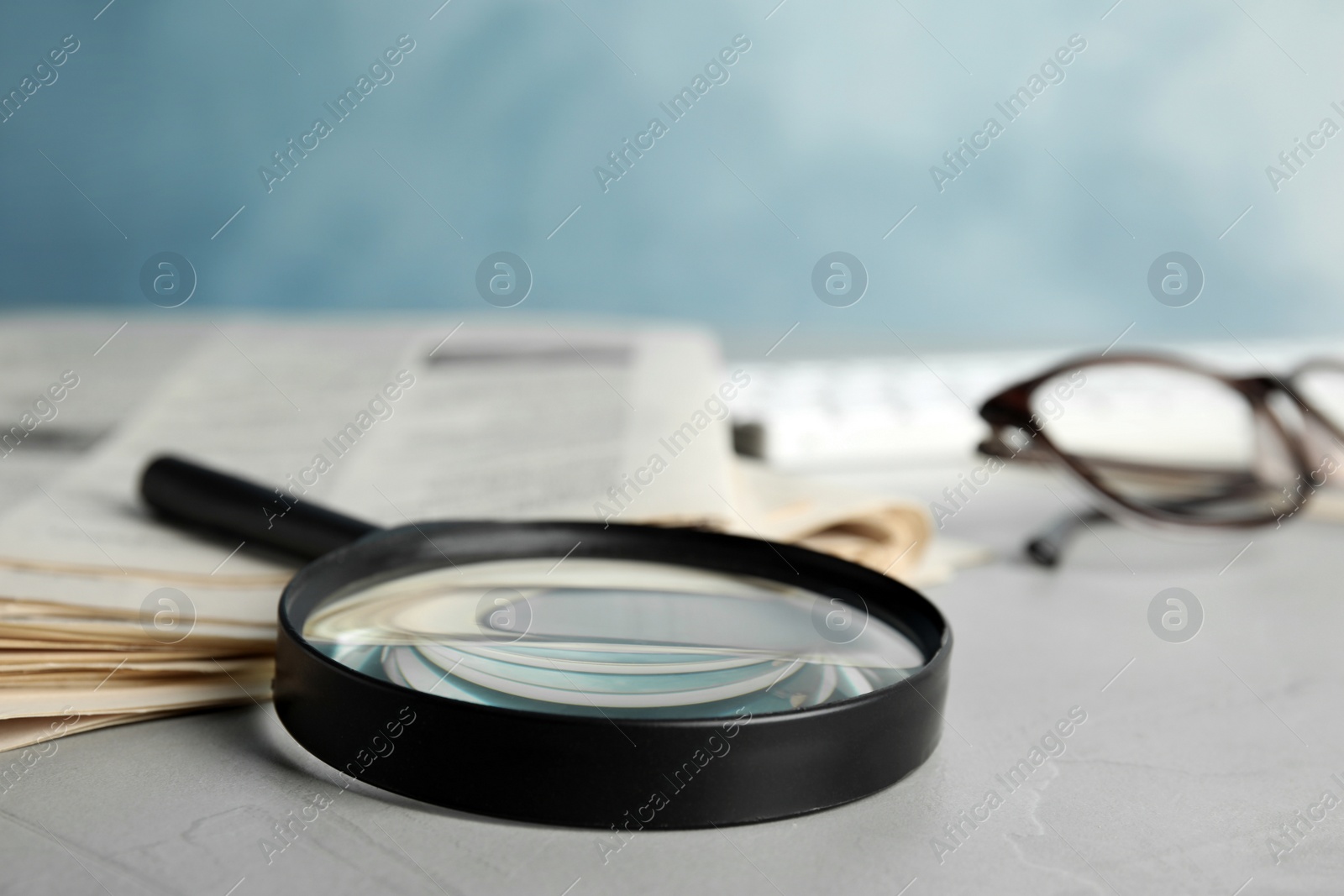Photo of Magnifying glass and stack of newspapers on grey table. Job search concept