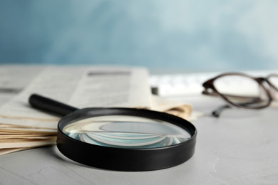 Magnifying glass and stack of newspapers on grey table. Job search concept