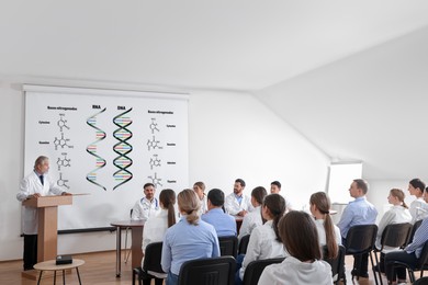Image of Lecture about difference between RNA and DNA. Professors and audience in conference room. Projection screen with illustration