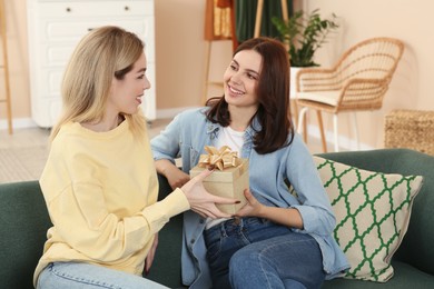 Smiling young woman presenting gift to her friend at home