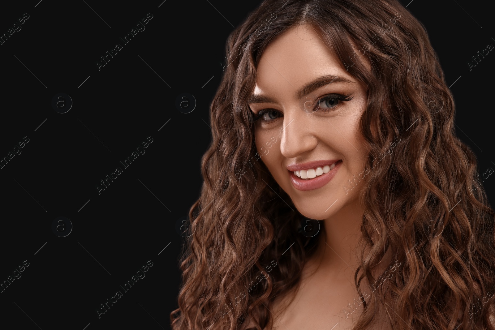 Photo of Beautiful young woman with long curly brown hair on black background, closeup. Space for text