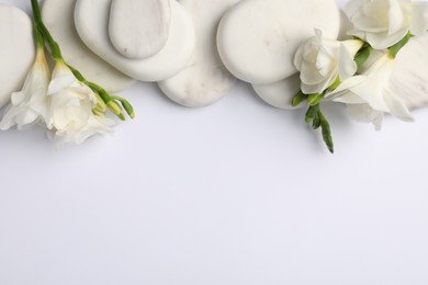 Photo of Flat lay composition with spa stones and freesia flowers on white background, space for text