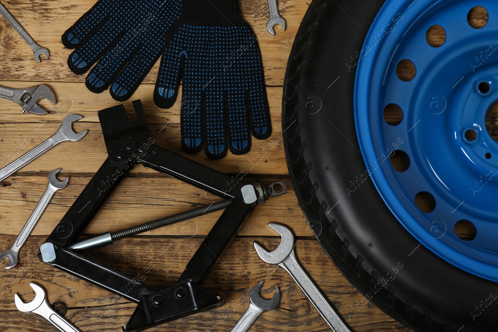 Photo of Car wheel, scissor jack, gloves and different tools on wooden surface, flat lay