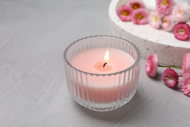 Photo of Stylish tender composition with burning candle and flowers on grey table. Cozy interior element