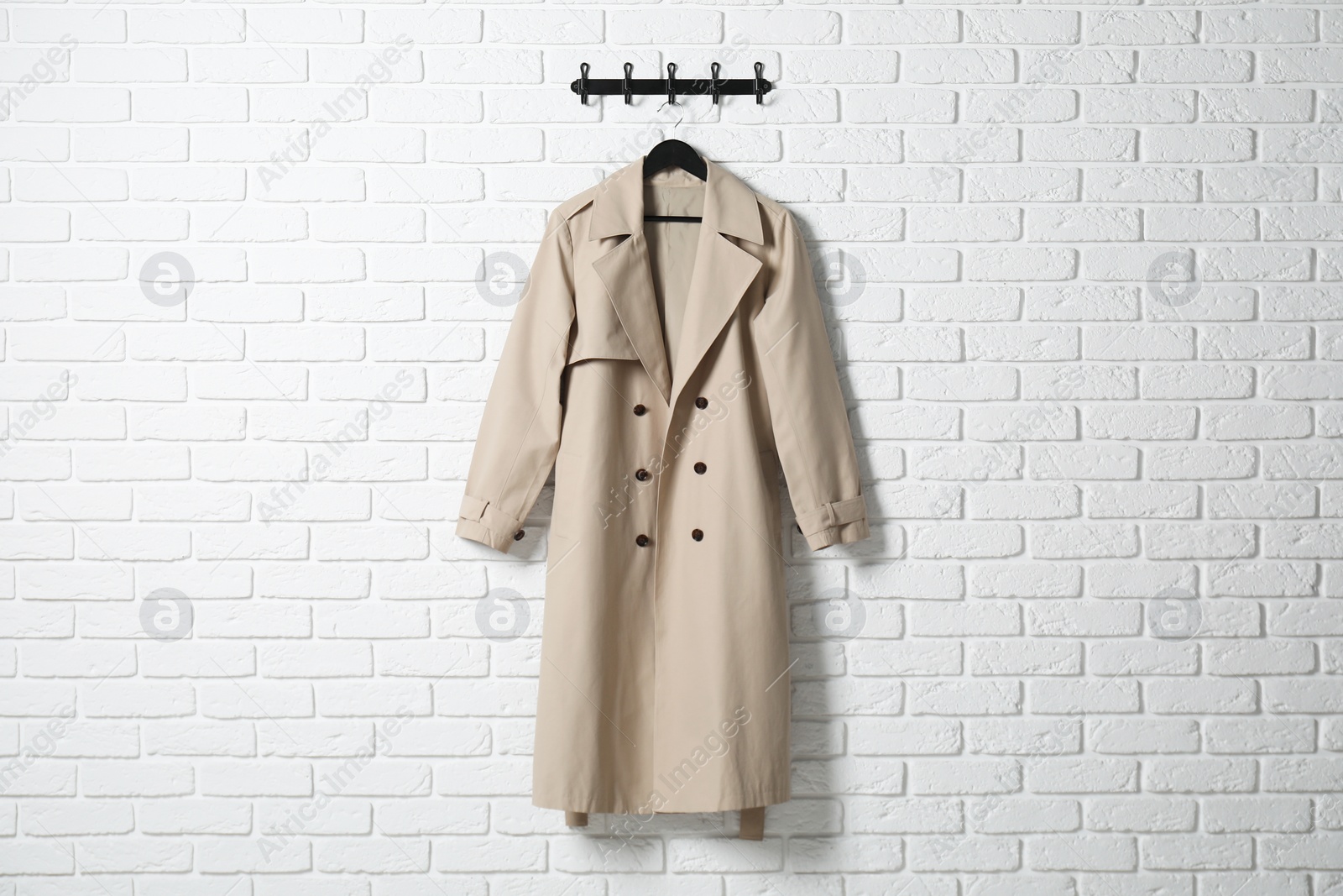 Photo of Hanger with beige coat on white brick wall