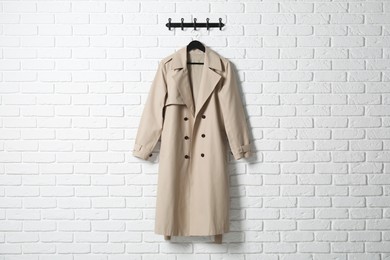 Hanger with beige coat on white brick wall