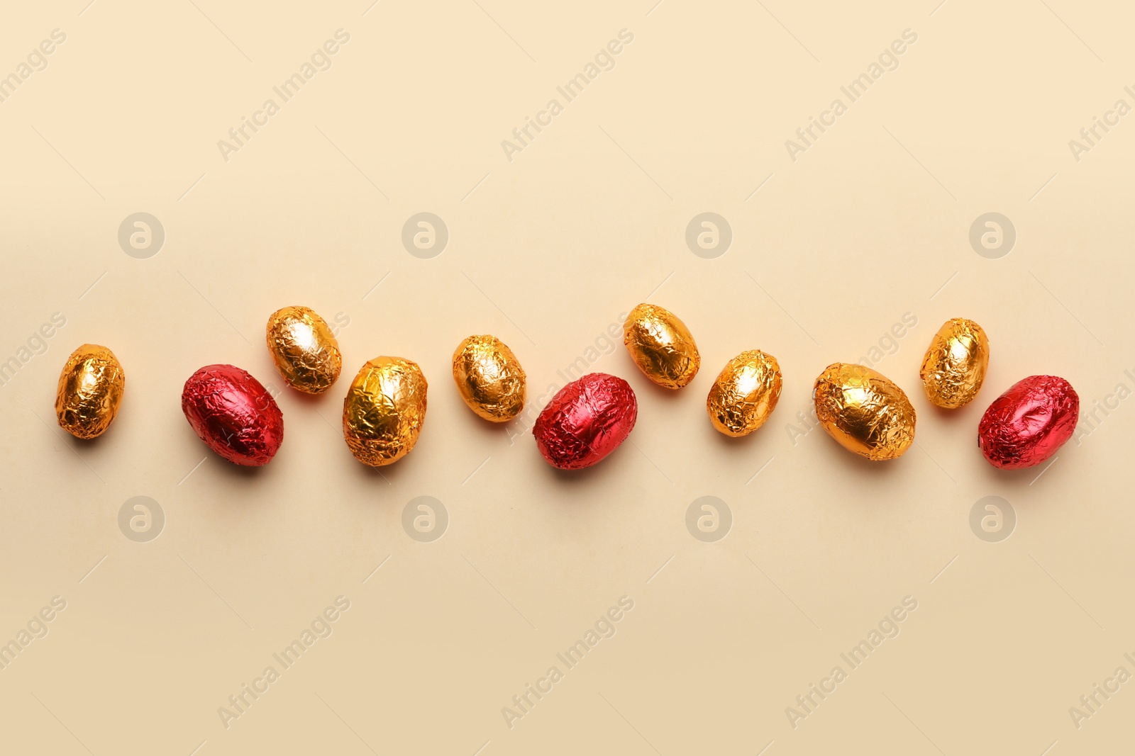 Photo of Chocolate eggs wrapped in red and golden foil on beige background, flat lay
